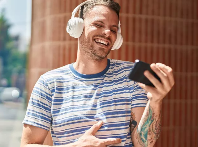 Un ragazzo sorridendo guarda lo smartphone simboleggiando la facilità con cui gli utilizzatori trovano i locali convenzionati sull’App